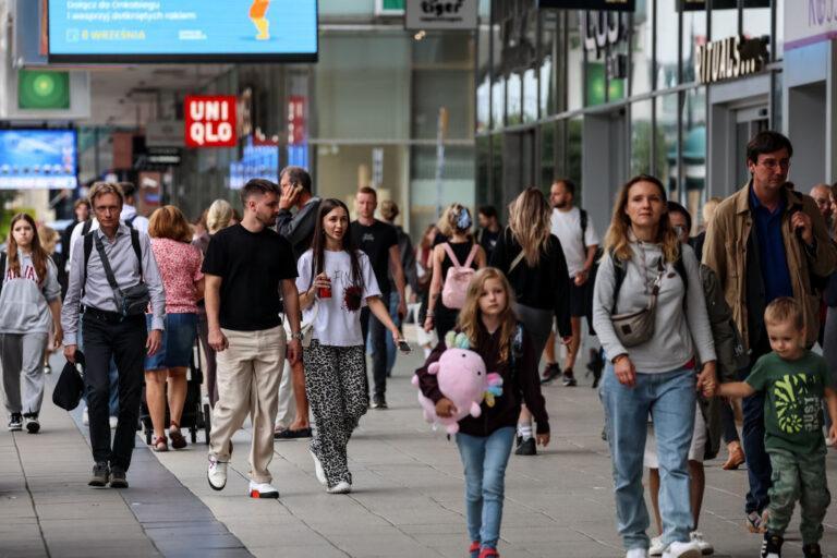 Zdjęcie przedstawia ludzi idących wzdłuż domów towarowych na ulicy Marszałkowskiej w Warszawie