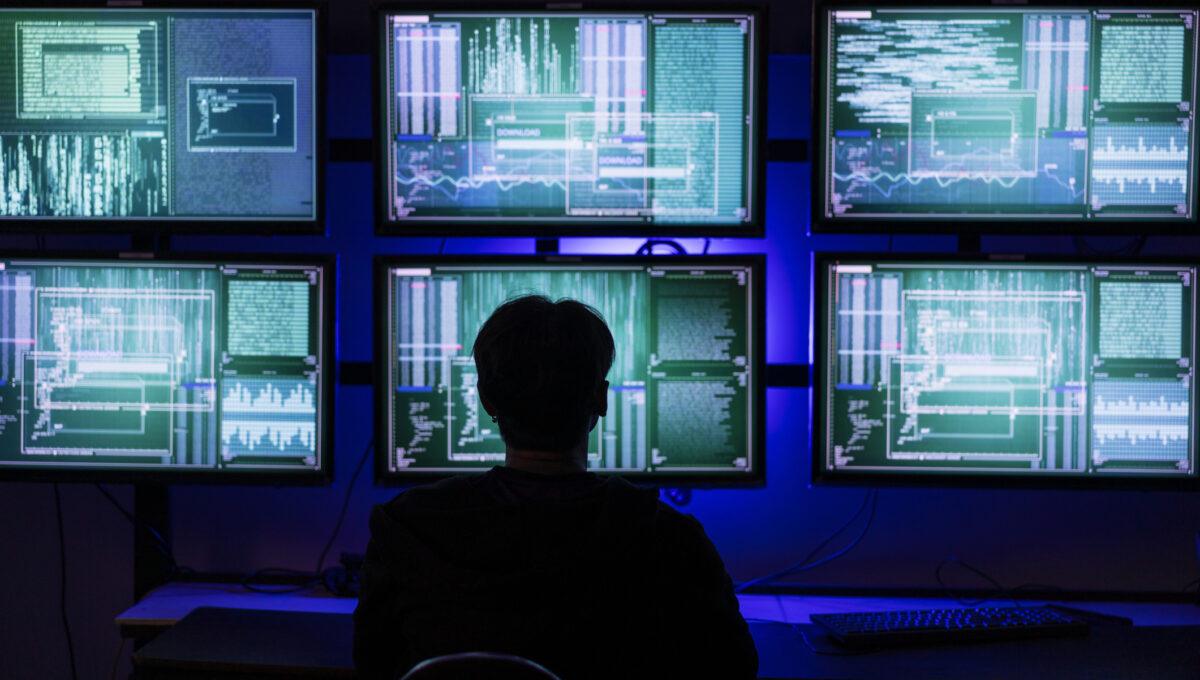 Na zdjęciu postać na tle monitorów