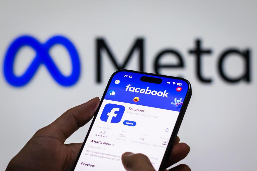 Aplikacja Facebook na telefonie, w tle logo spółki Meta