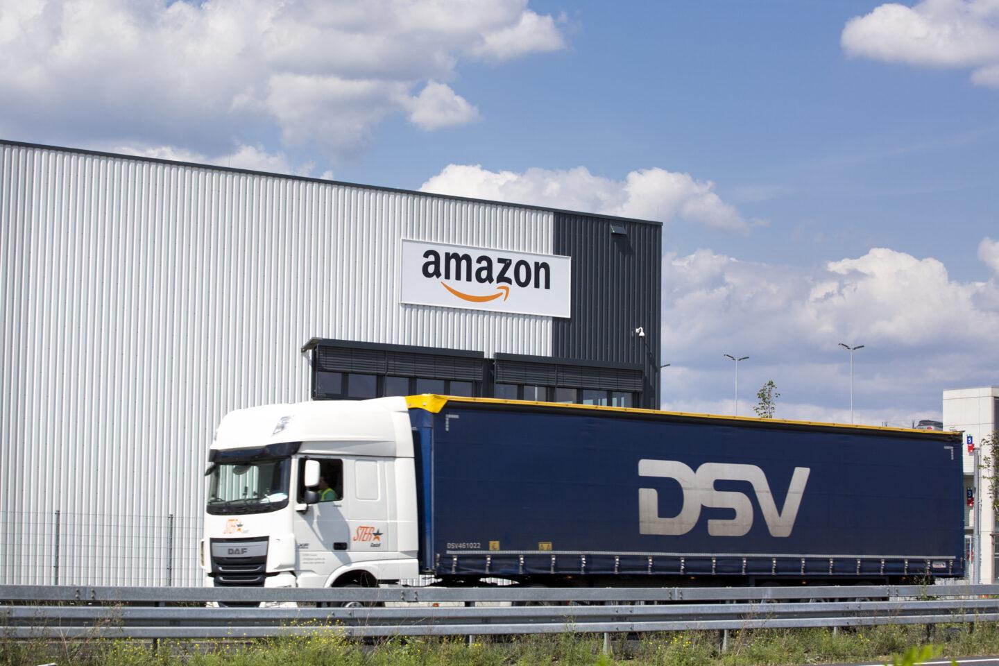 Na zdjęciu samochód ciężarowy firmy DSV na tle magazyny z logo Amazona.