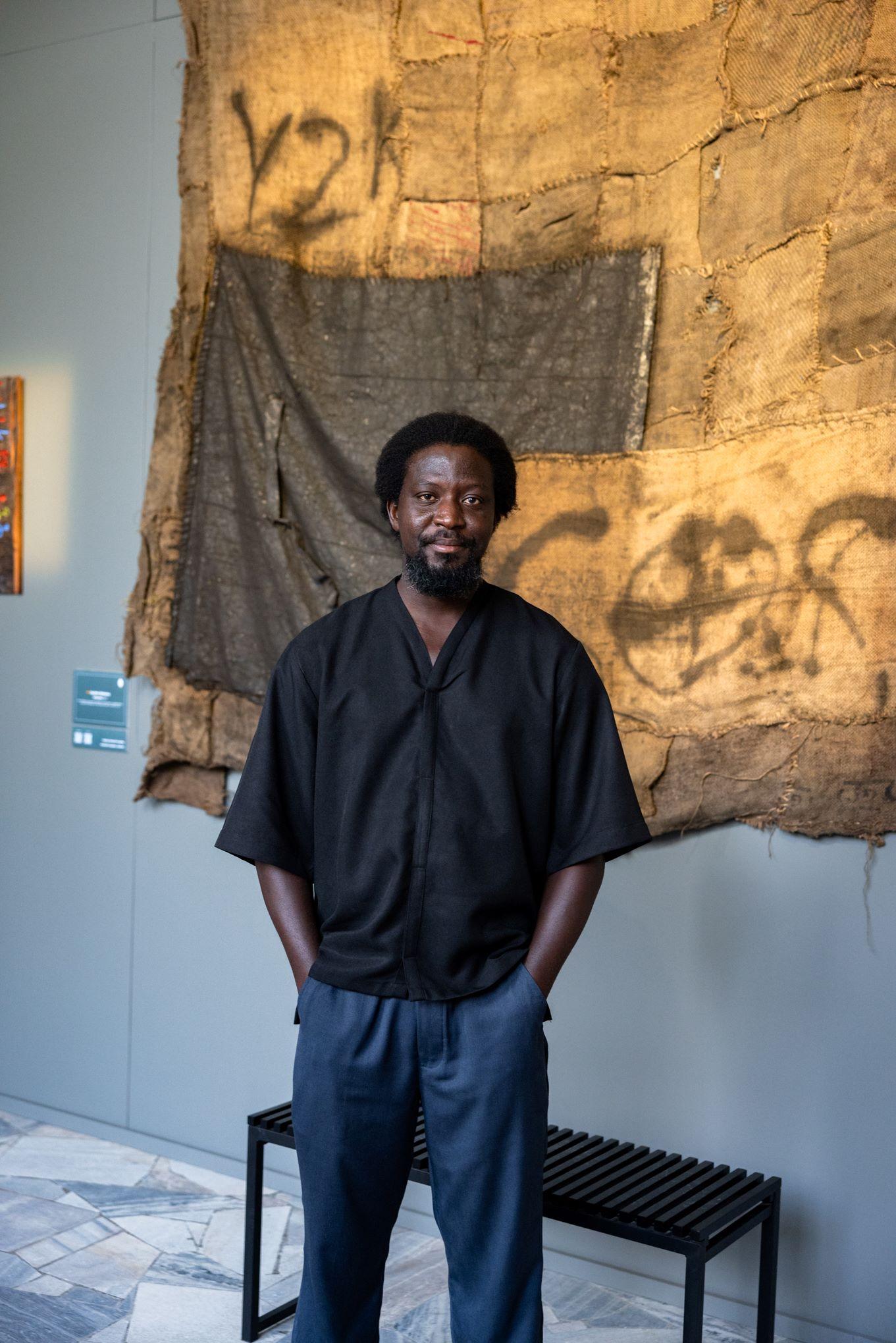 Ibrahim Mahama na tle swojej pracy z worka jutowego. Fot Alex Dolny