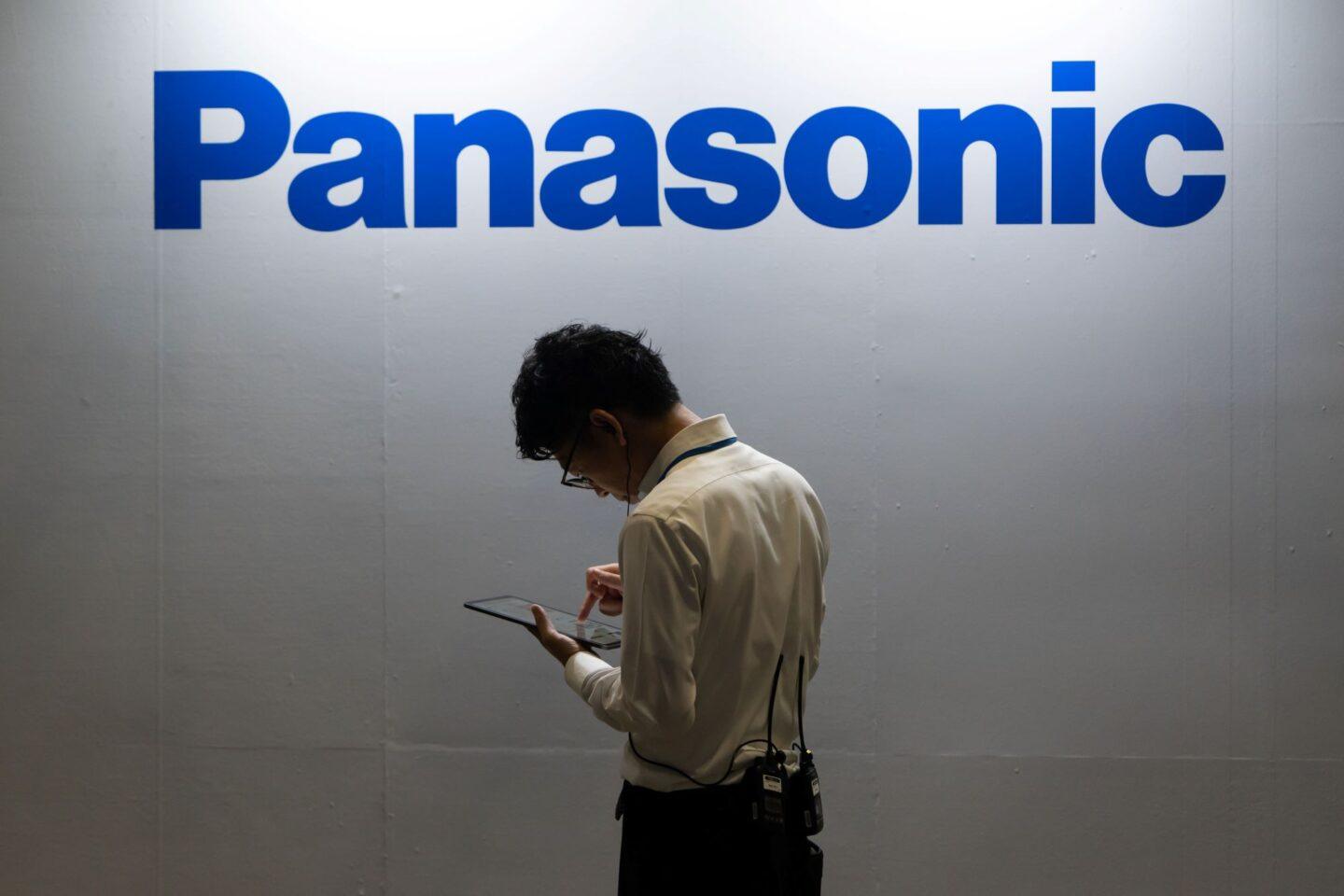Zdjęcie przedstawia osobę trzymającą telefon na tle logo firmy Panasonic
