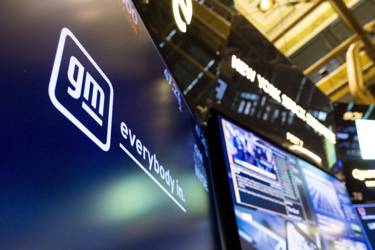 Zdjęcie przedstawia logo General Motors (GM) na tle ekranu na giełdzie NYSE na Wall Street