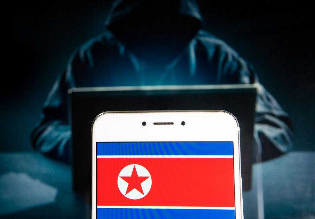 Na ilustracji flaga Korei Północnej na tle zakapturzonej postaci przed komputerem