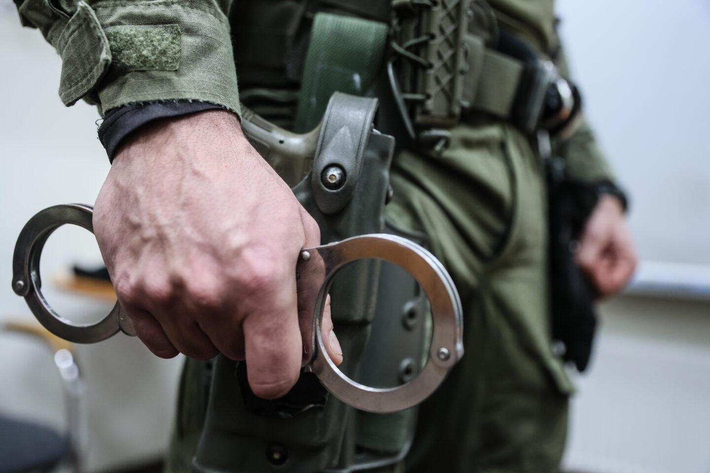Na zdjęciu zamaskowany funkcjonariusz CBŚP trzyma w dłoni kajdanki