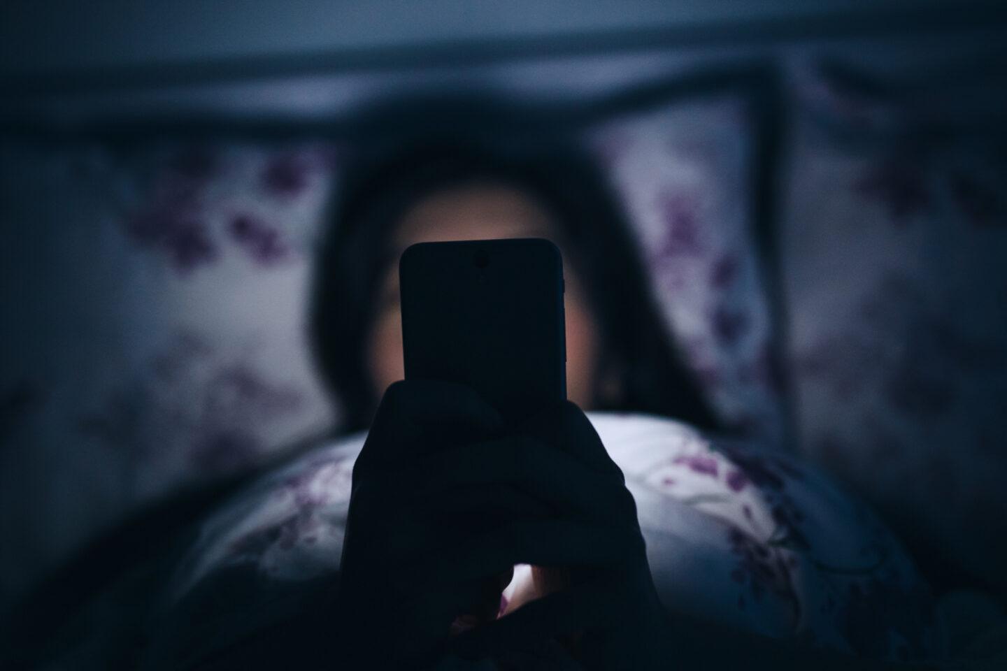 Na zdjęciu kobieta korzystająca ze smartfona późno w nocy