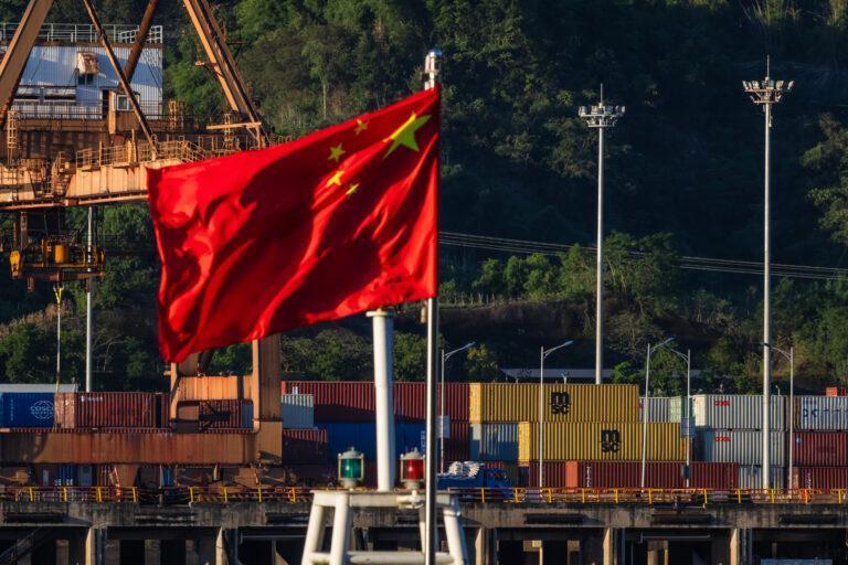 Na pierwszym planie widać chińską flagę, w tle znajdują się kontenery wykorzystywane w transporcie morskim