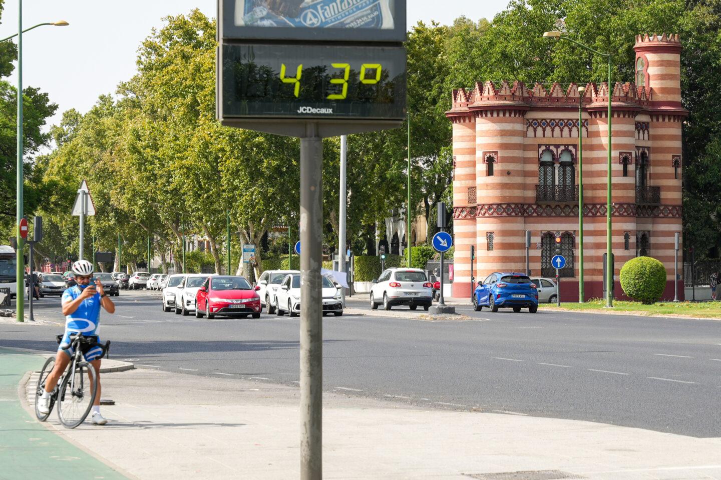 Na zdjęciu rowerzysta robi zdjęcie ulicznego termometru wskazującego temperaturę 43 stopni Celsjusza w Sewilli
