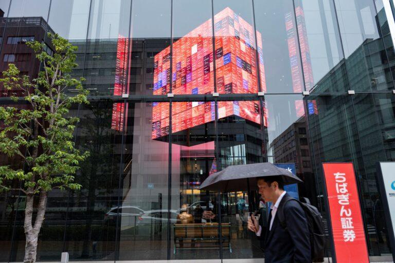 Zdjęcie przedstawia mężczyznę z parasolką przed budynkiem giełdy w Tokio w Japonii