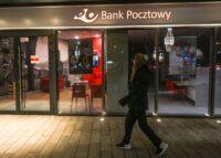 Zdjęcie przedstawia kobietę przed placówką Banku Pocztowego