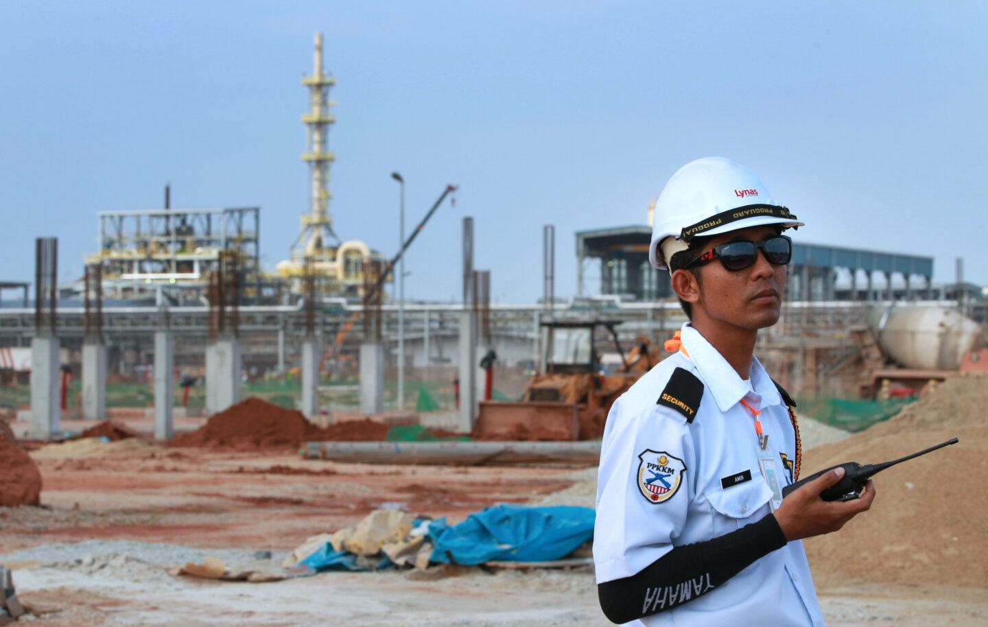 Mężczyzna w kasku i mundurze stoi na tle obiektów przemysłowych