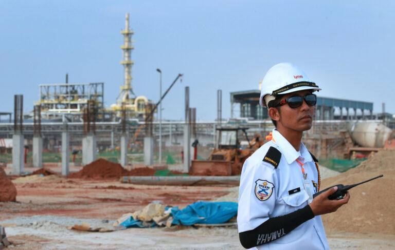 Mężczyzna w kasku i mundurze stoi na tle obiektów przemysłowych