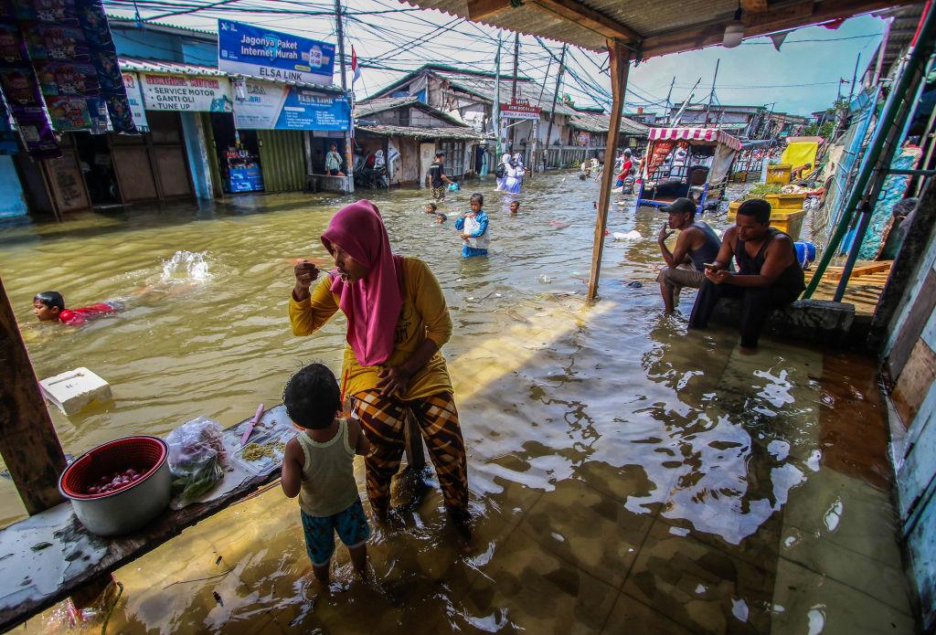 Na pierwszym planie kobieta w różowym hidżabie na tle podtopionej ulicy handlowej
