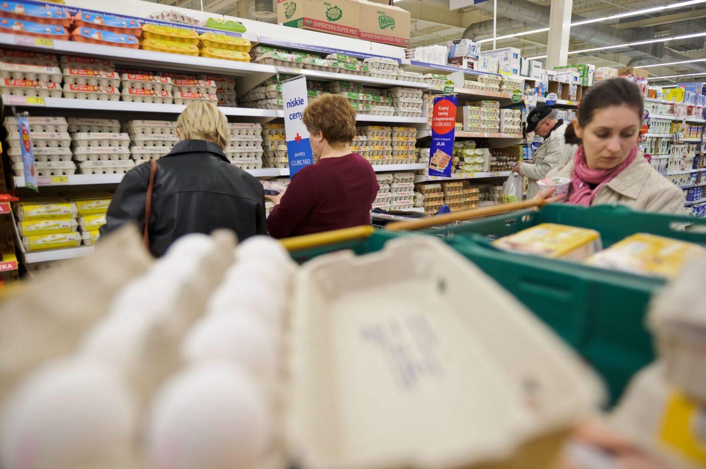 Zdjęcie przedstawia wytłaczankę jajek na tle osób robiących zakupy w supermarkecie
