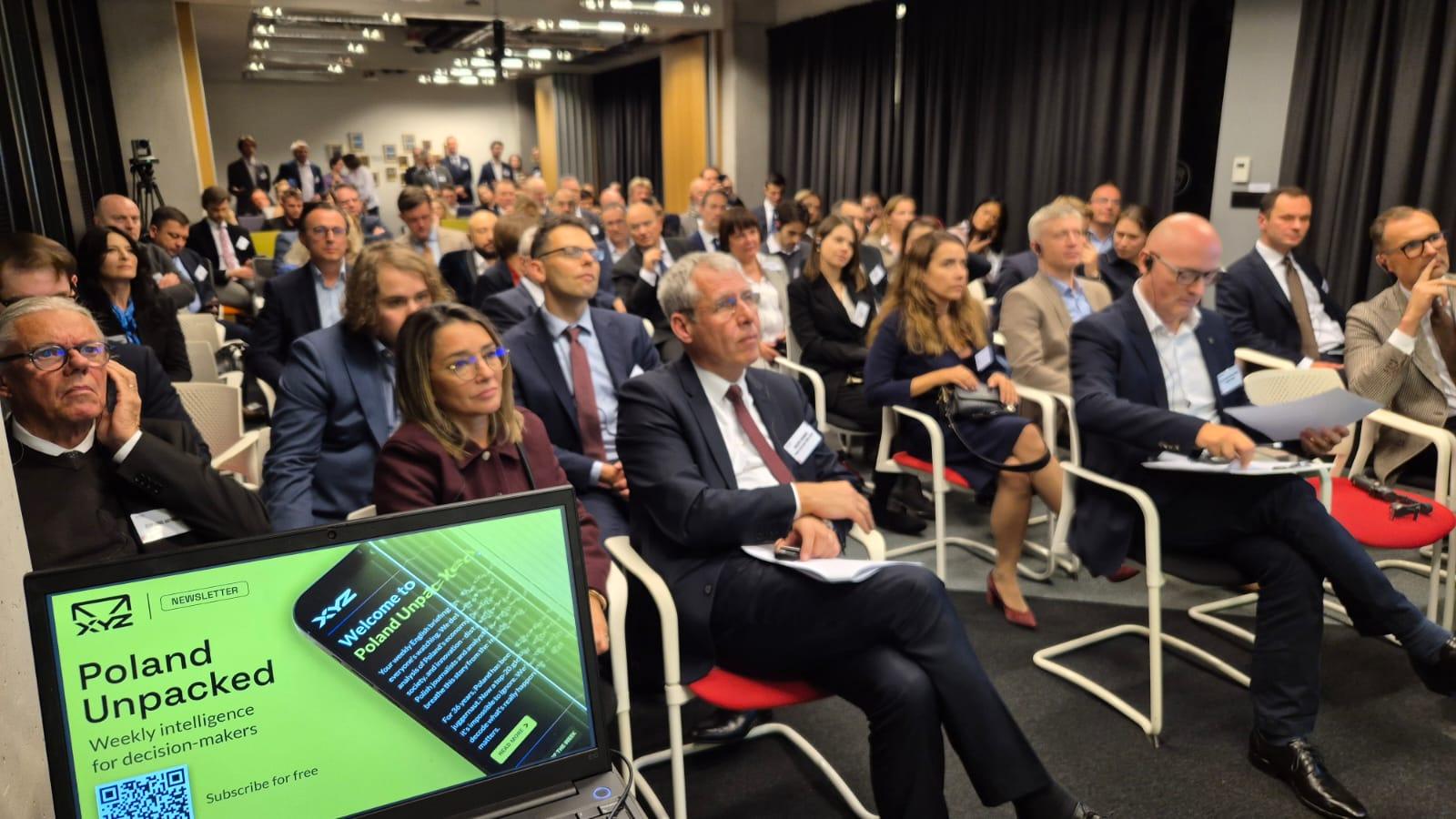 Na zdjęciu uczestnicy debaty i ekran z napisem Poland Unpacked