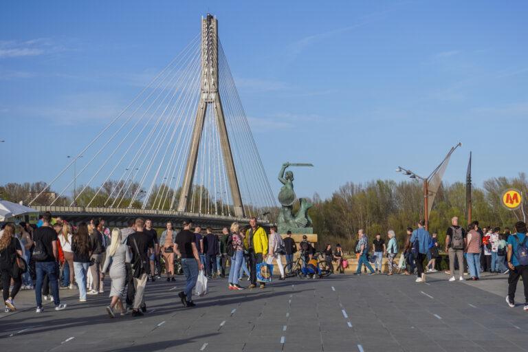 Przechodnie w Warszawie, przy Pomniku Syrenki nad Wisłą. W tle Most Świętokrzyski