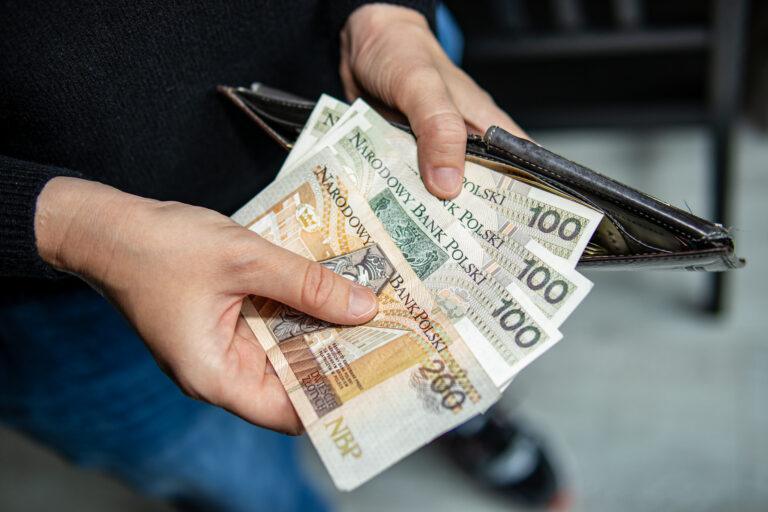 Hands holding 100 and 200 Polish zloty banknotes above an open wallet. Concept of income, spending, personal finance, or budgeting