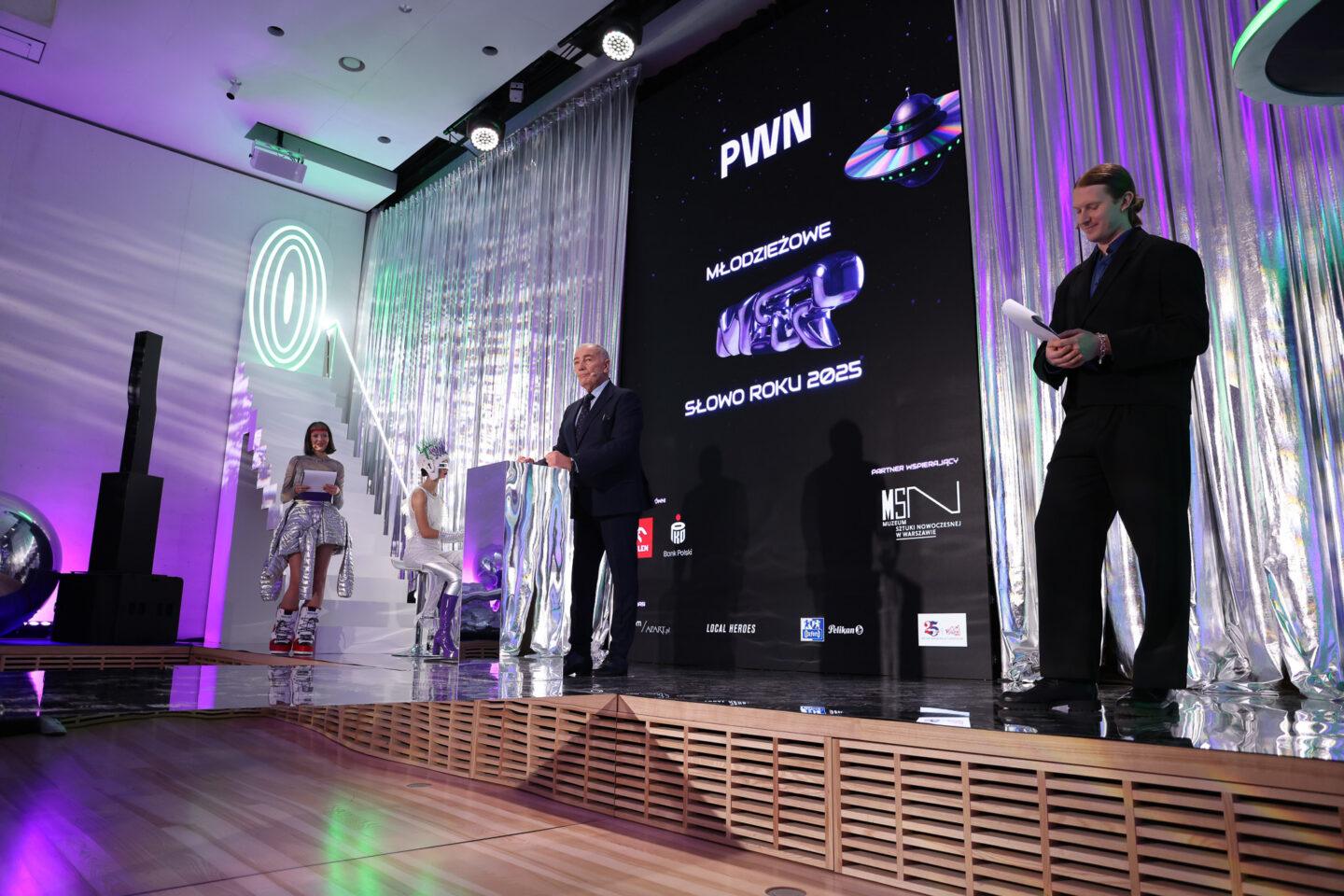 Zdjęcie przedstawia galę finałową plebiscytu PWN Młodzieżowe Słowo Roku 2025. Na zdjęciu w centrum aktor i prezenter medialny Karol Strasburger