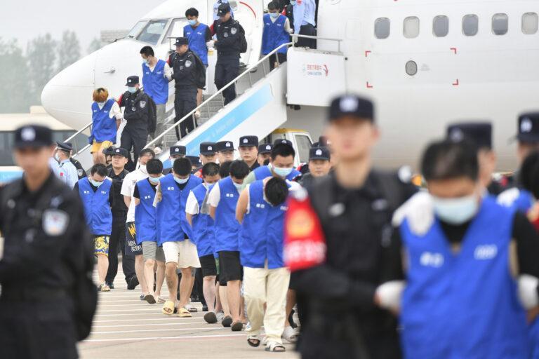 Grupa osób w niebieskich uniformach eskortowana przez policjantów