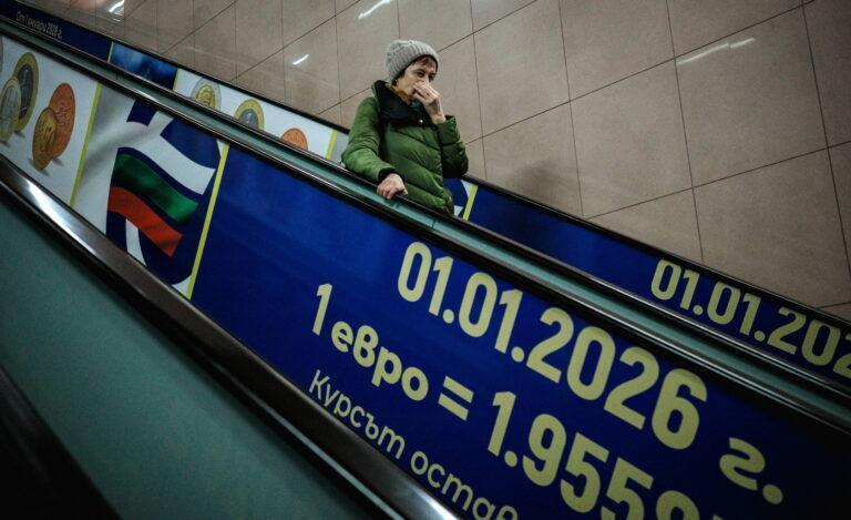 Kobieta zjeżdża po ruchomych schodach, na których widnieje plakat promujący przyjęcie euro w Bułgarii.