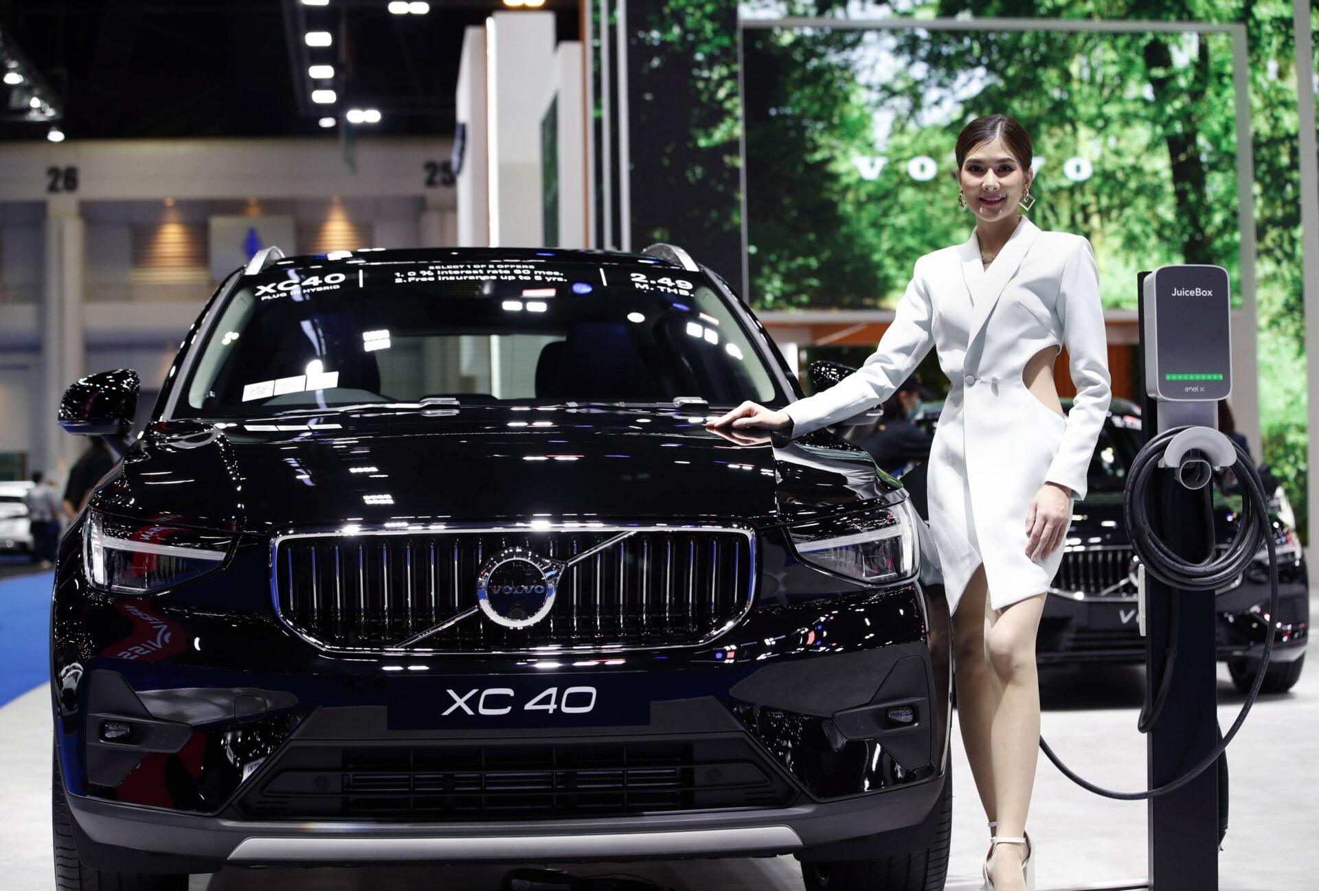 Kobieta w białym kostiumie stoi obok elektrycznego auta