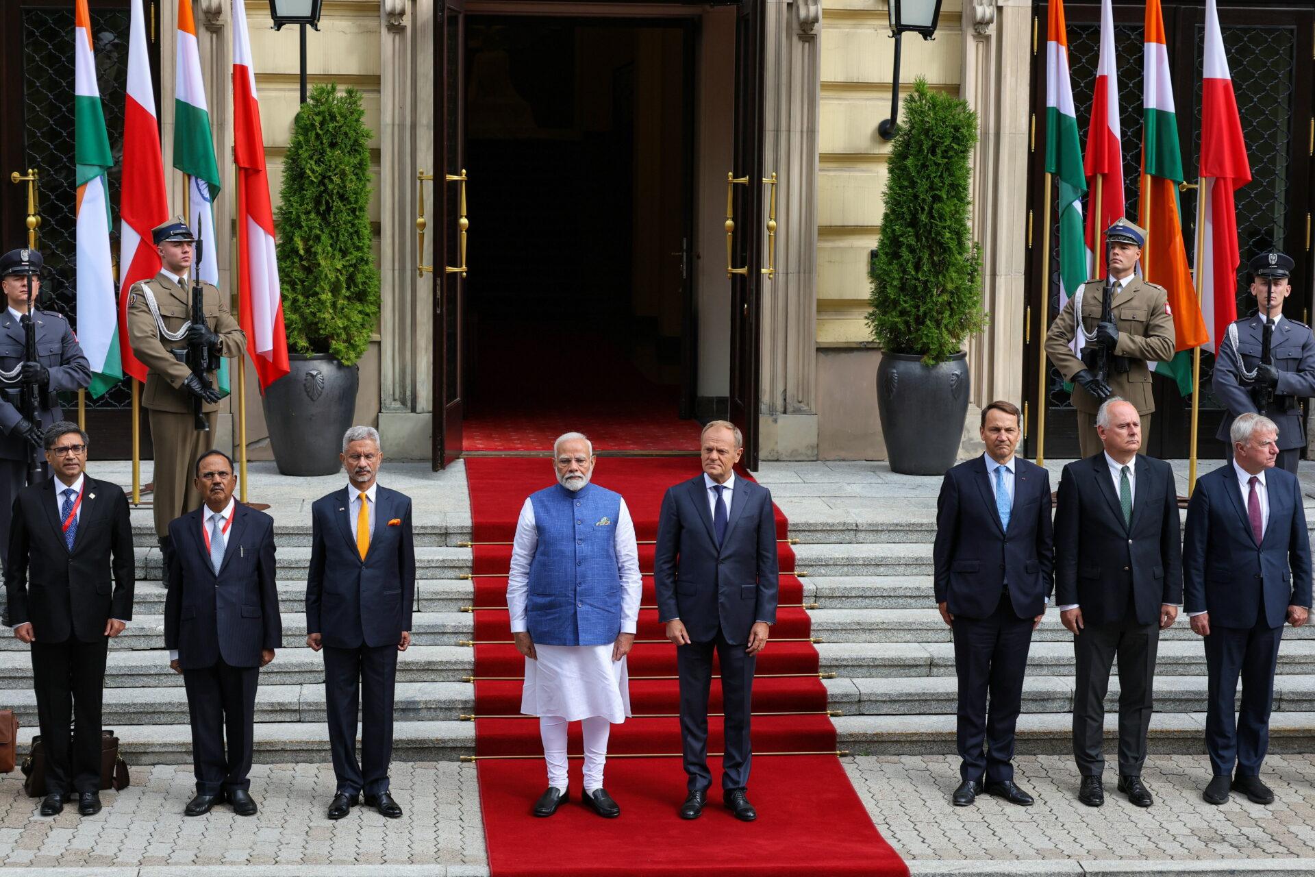 Grupa osób przed budynkiem, na tle flag Polski i Indii