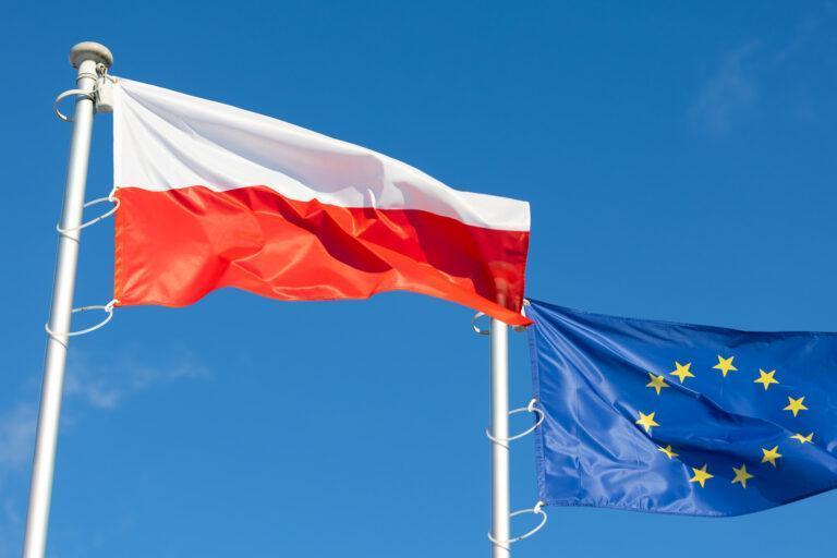 The flags of Poland and the European Union waving against the blue sky