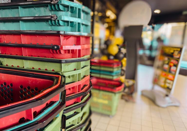 Colorful plastic shopping baskets stacked in a supermarket, retail store equipment symbolizing shopping, consumerism, retail industry and modern commerce background