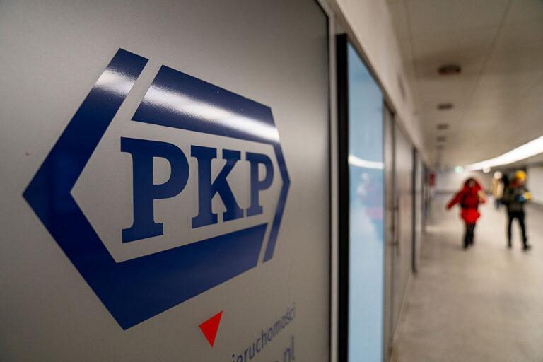 Logo PKP a w tle ludzie na dworcu