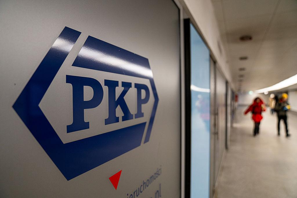 Logo PKP a w tle ludzie na dworcu