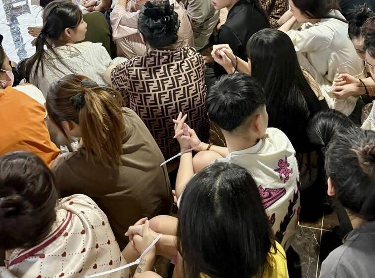 Grupa osób ze związanymi rękami siedzi na podłodze