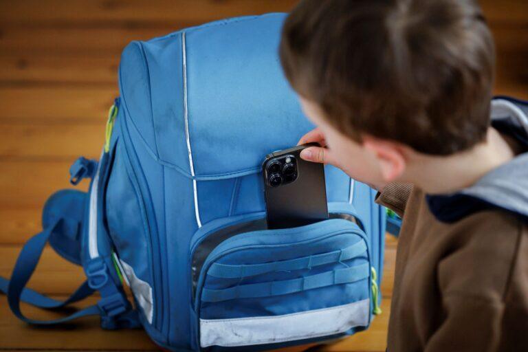 Dziecko wkładające smartfon do plecaka szkolnego