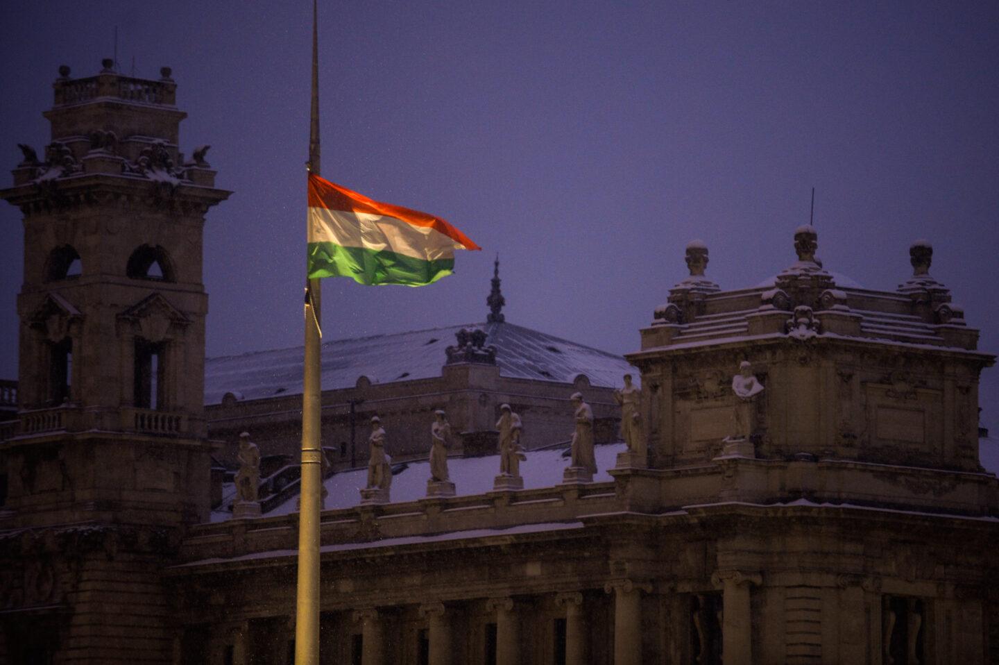 Węgierska flag na tle ogarniętego wieczornym mrokiem, ośnieżonego gmachu parlamentu w Budapeszcie.