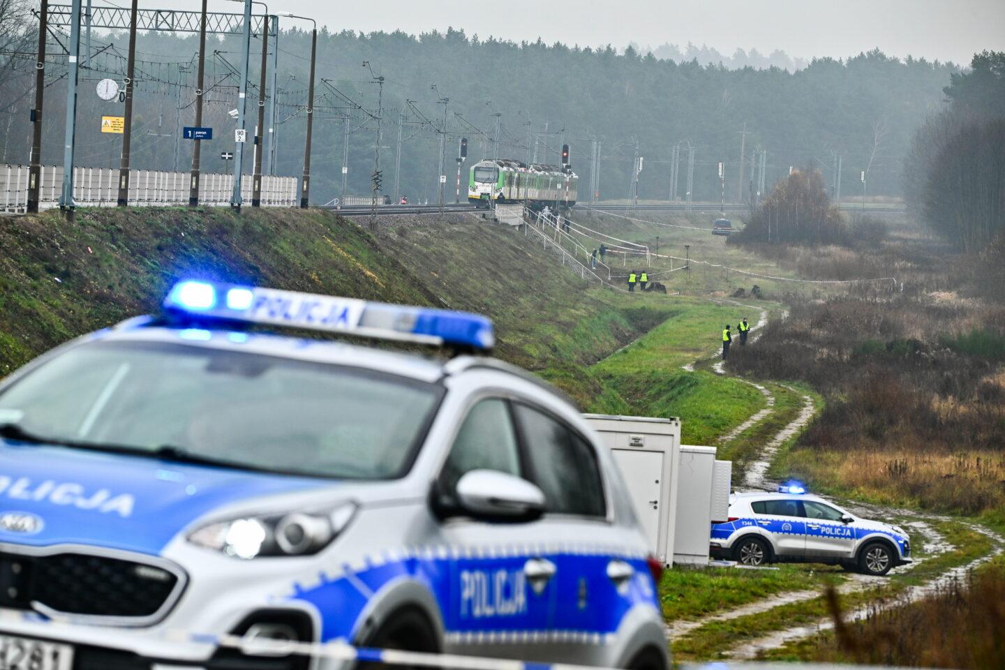 Radiowozy policyjne na tle torów kolejowych i pociągu