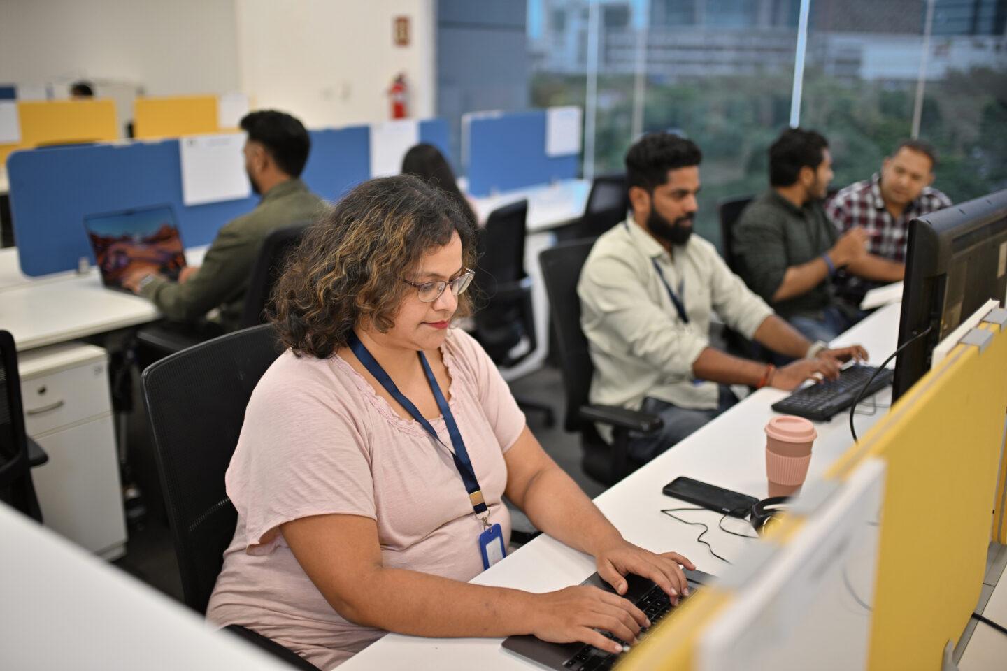 Kobieta w towarzystwie współpracowników pracuje na komputerze