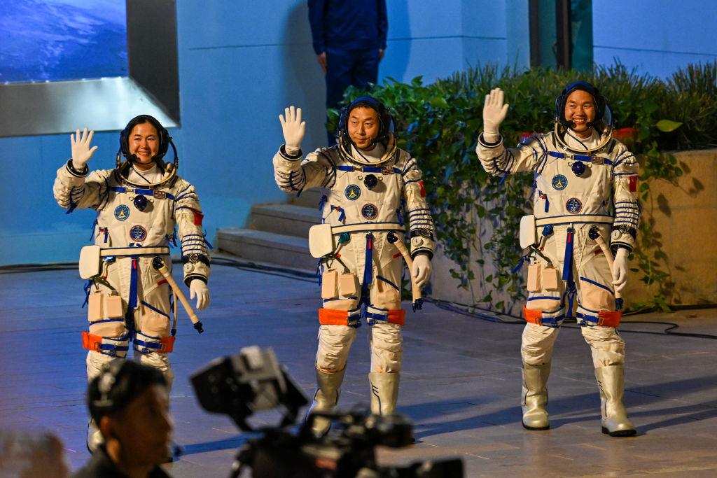 Trójka chińskich astronautów w skafandrach macha w kierunku kamery