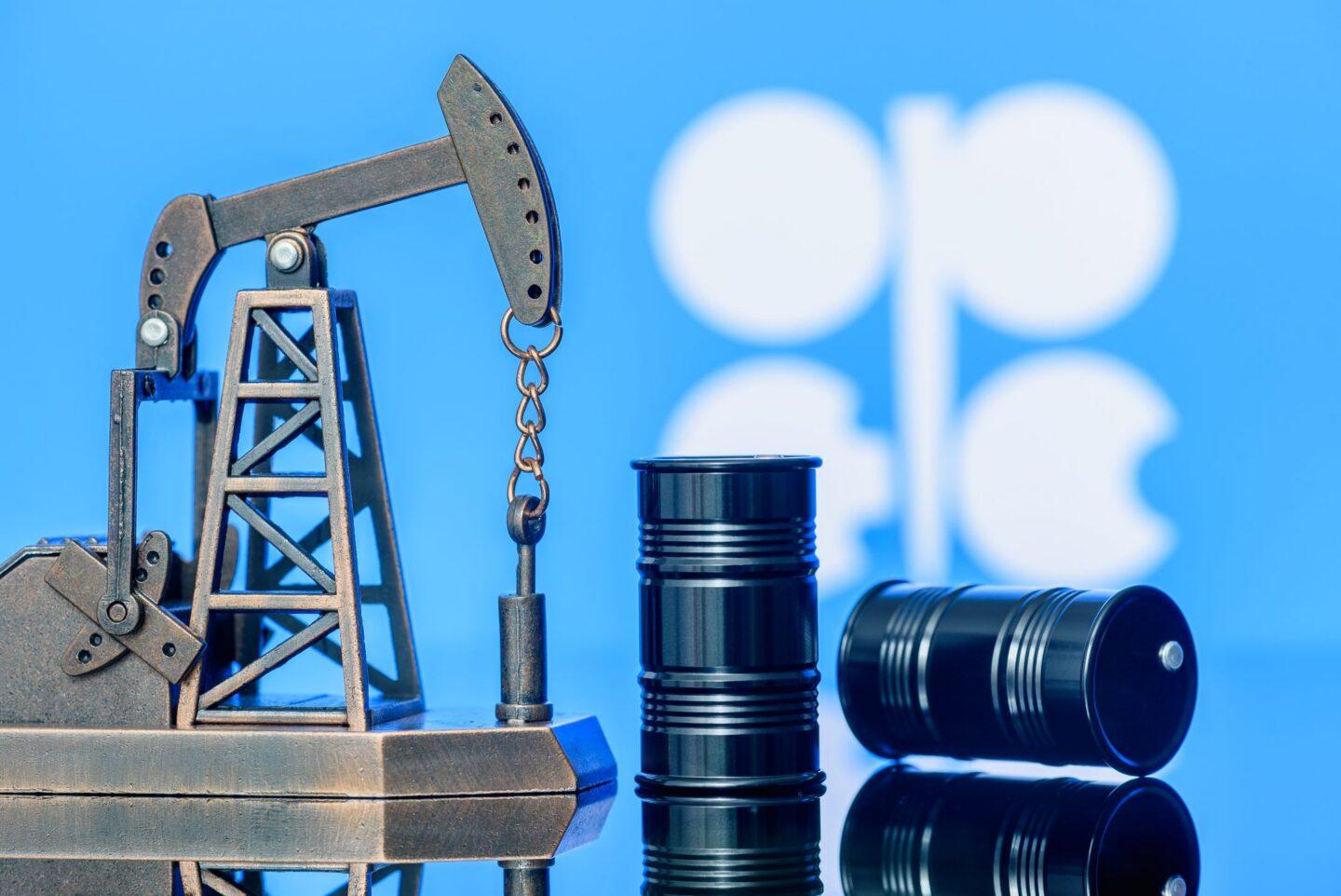 Baryłki ropy i szyb wiertniczy na tle flagi OPEC