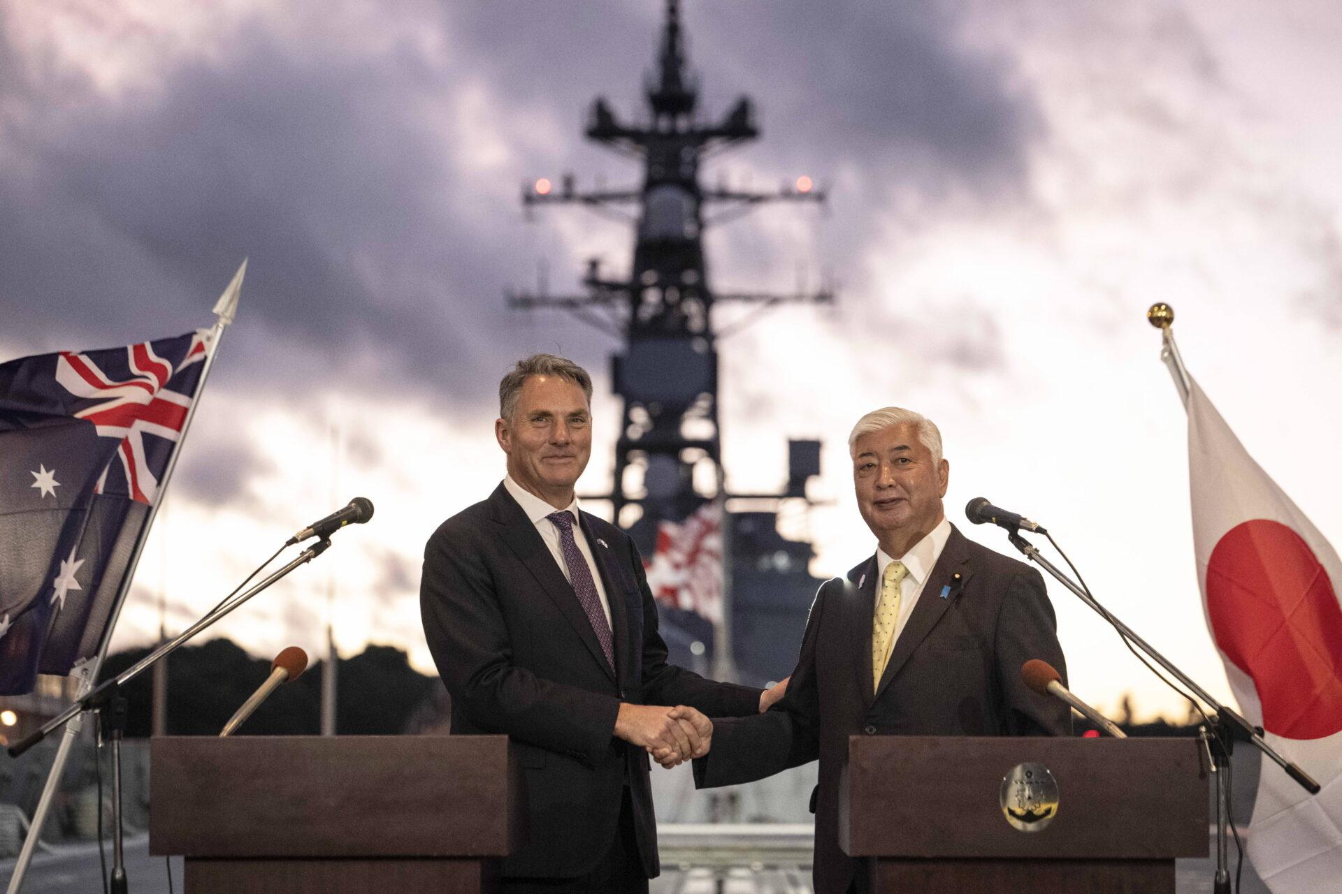 Ministrowie obrony Japonii Gen Nakatani i Australii Richard Marles ściskają sobie dłonie na pokładzie okrętu 