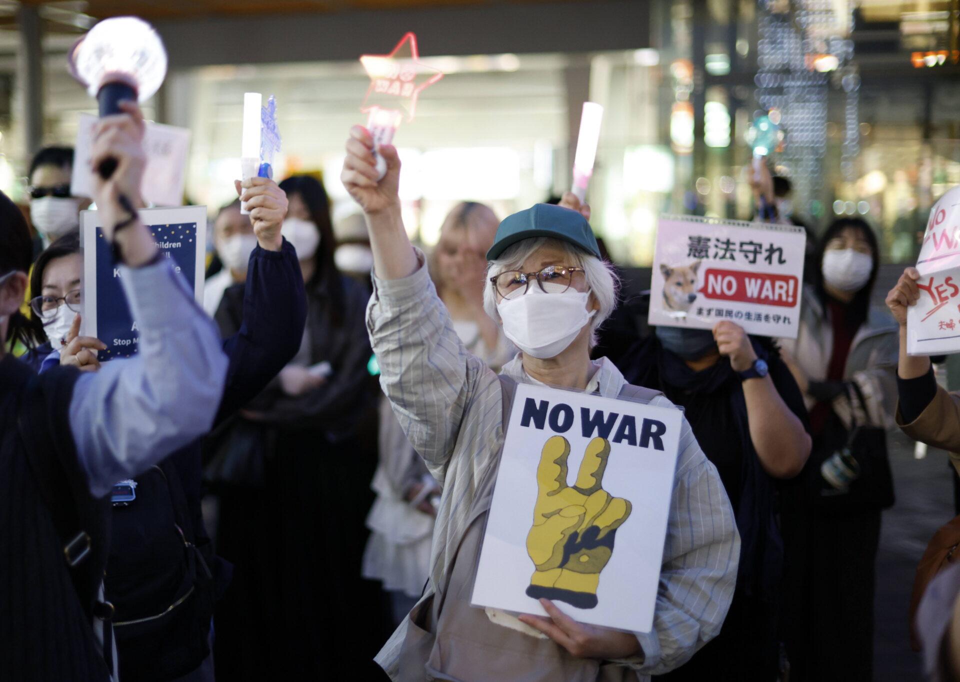 Grupa osób z antywojennymi banerami po angielsku i japońsku