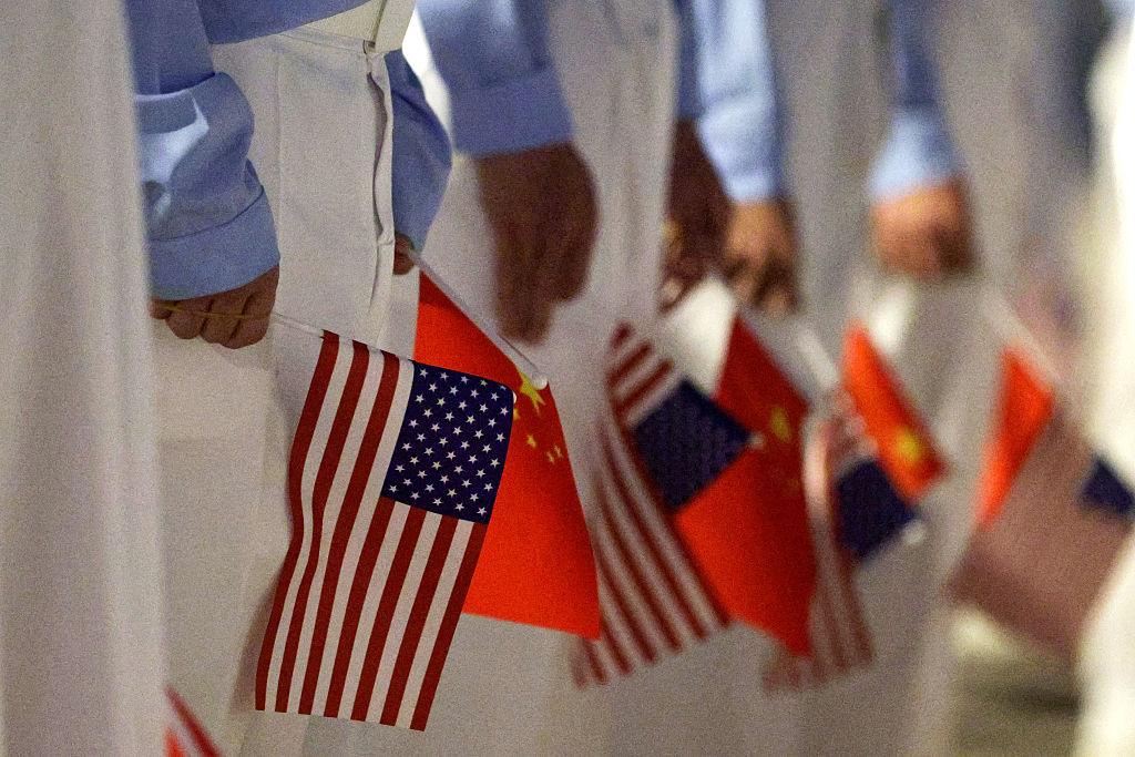 Grupa osób trzyma w rękach chorągiewki Chin i USA
