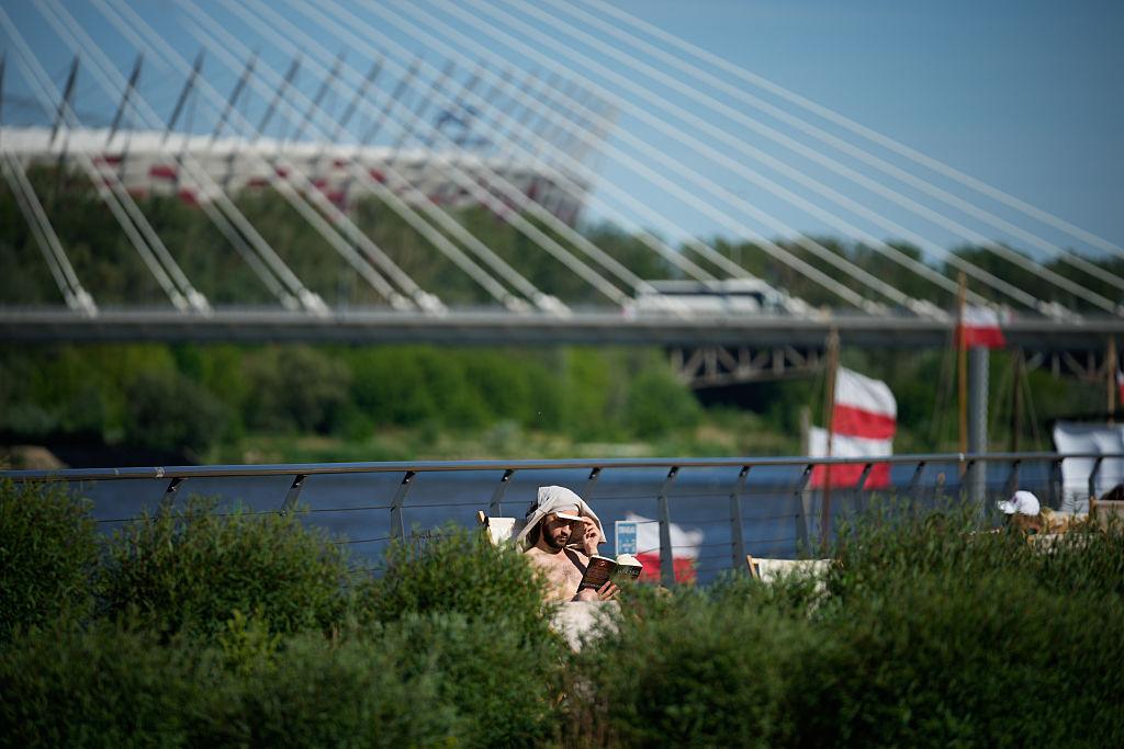 Mężczyzna czyta książkę na leżaku i chroni głowę koszulką przed słońcem na tle Stadionu Narodowego w Warszawie