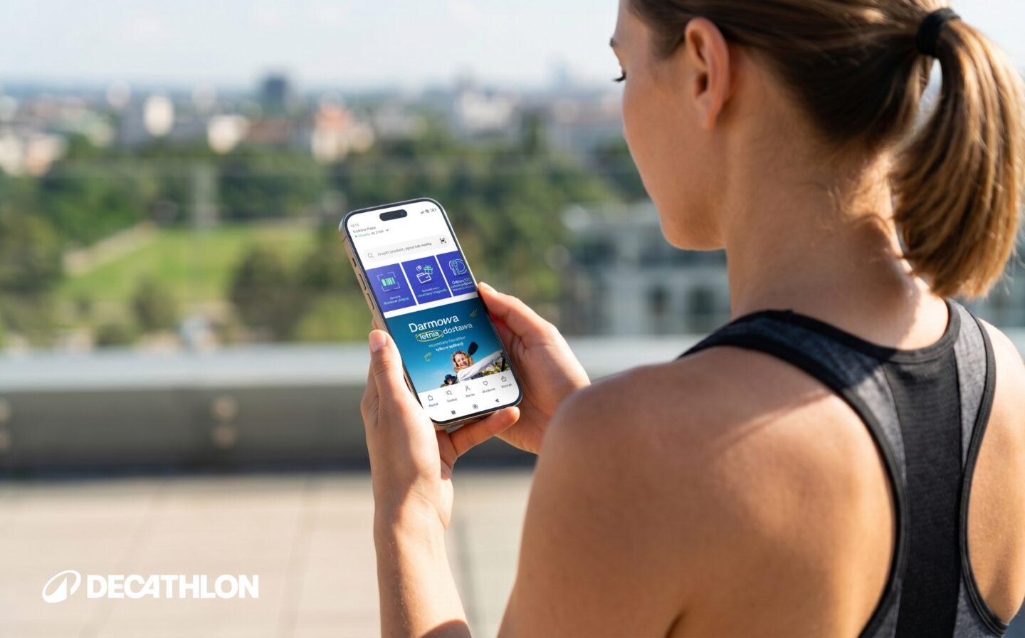 Kobieta ubrana w sportowy strój trzymająca telefon z otwartą aplikacją Decathlon