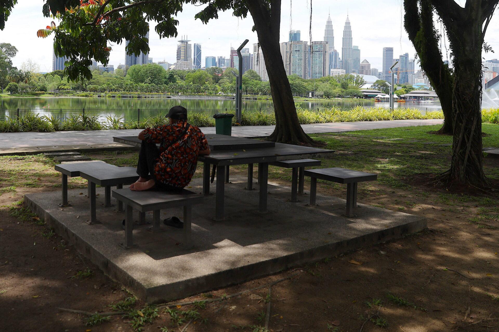 A man rests in a park near the capital city skyline in Kuala Lumpur, Malaysia,