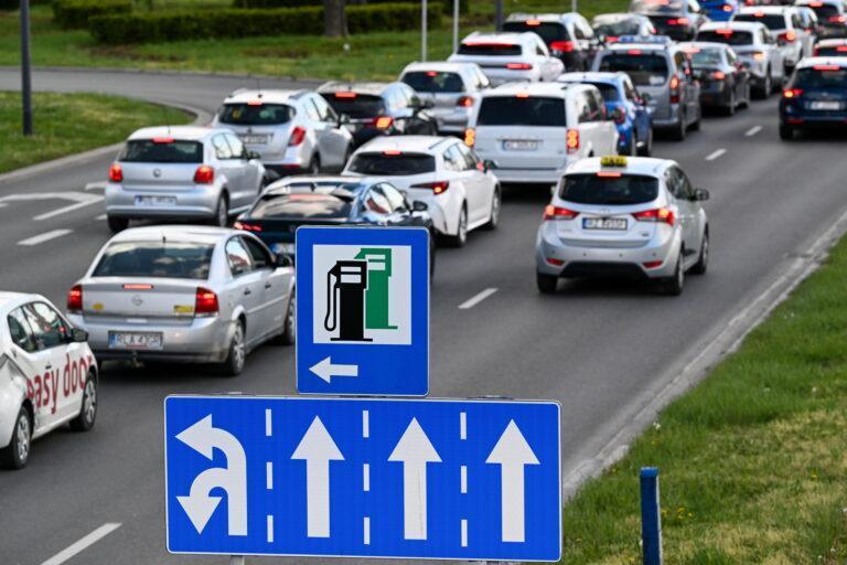 Ruch uliczny w Rzeszowie w tle, na pierwszym planie znak drogowy informujący o stacji benzynowej