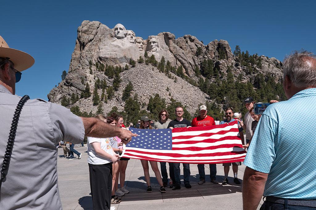 Ludzie z flagą amerykańską na tle głów prezydentów wykutych w Mount Rushmore