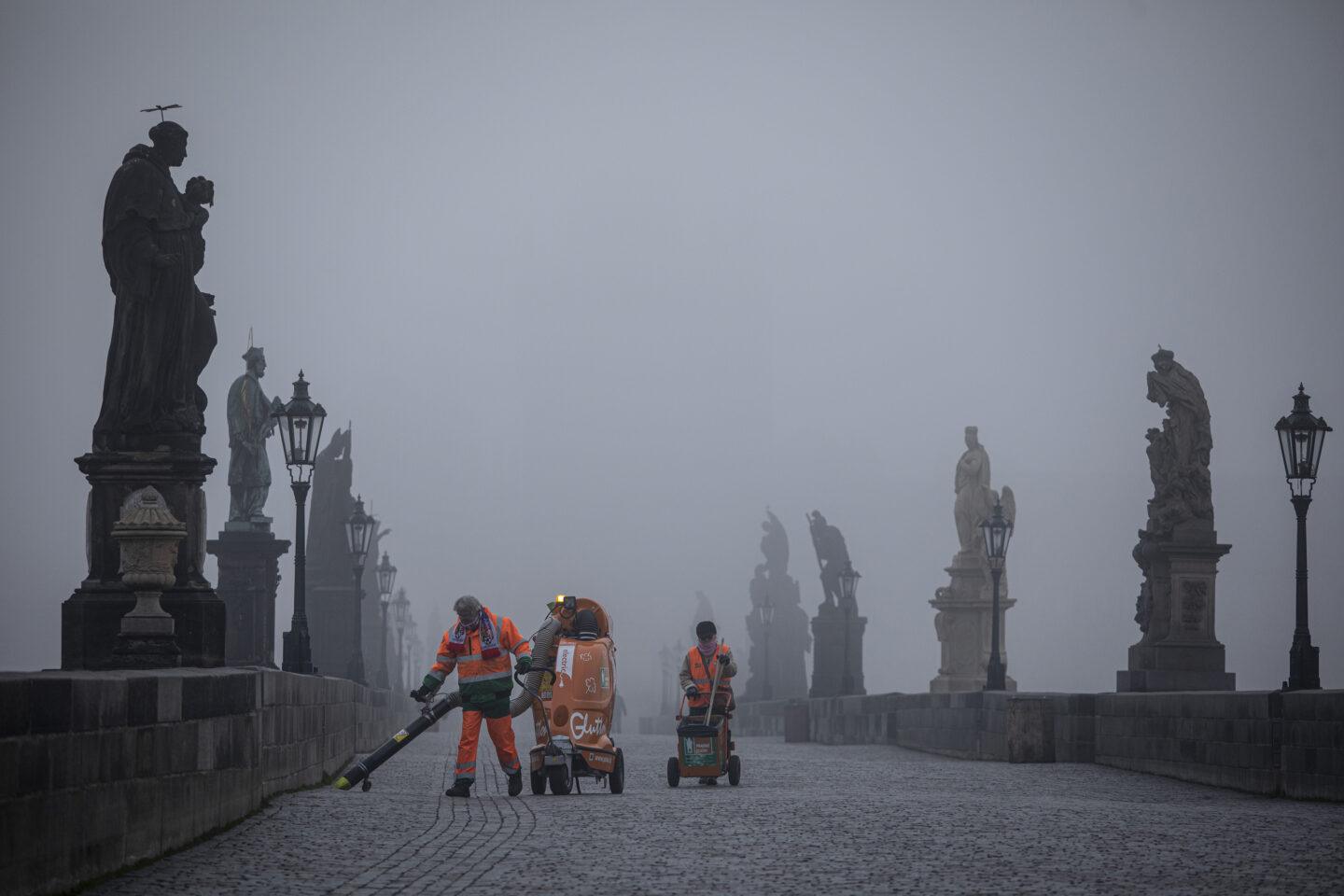 Pracownicy miejscy sprzątają pusty Most Karola o świcie w Pradze, w Czechach.