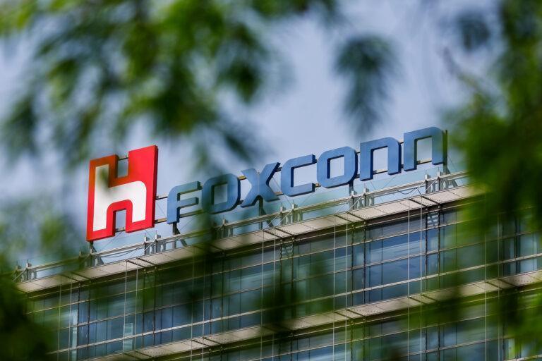 Logo międzynarodowej firmy technologicznej Foxconn na jej biurowcu wśród drzew.