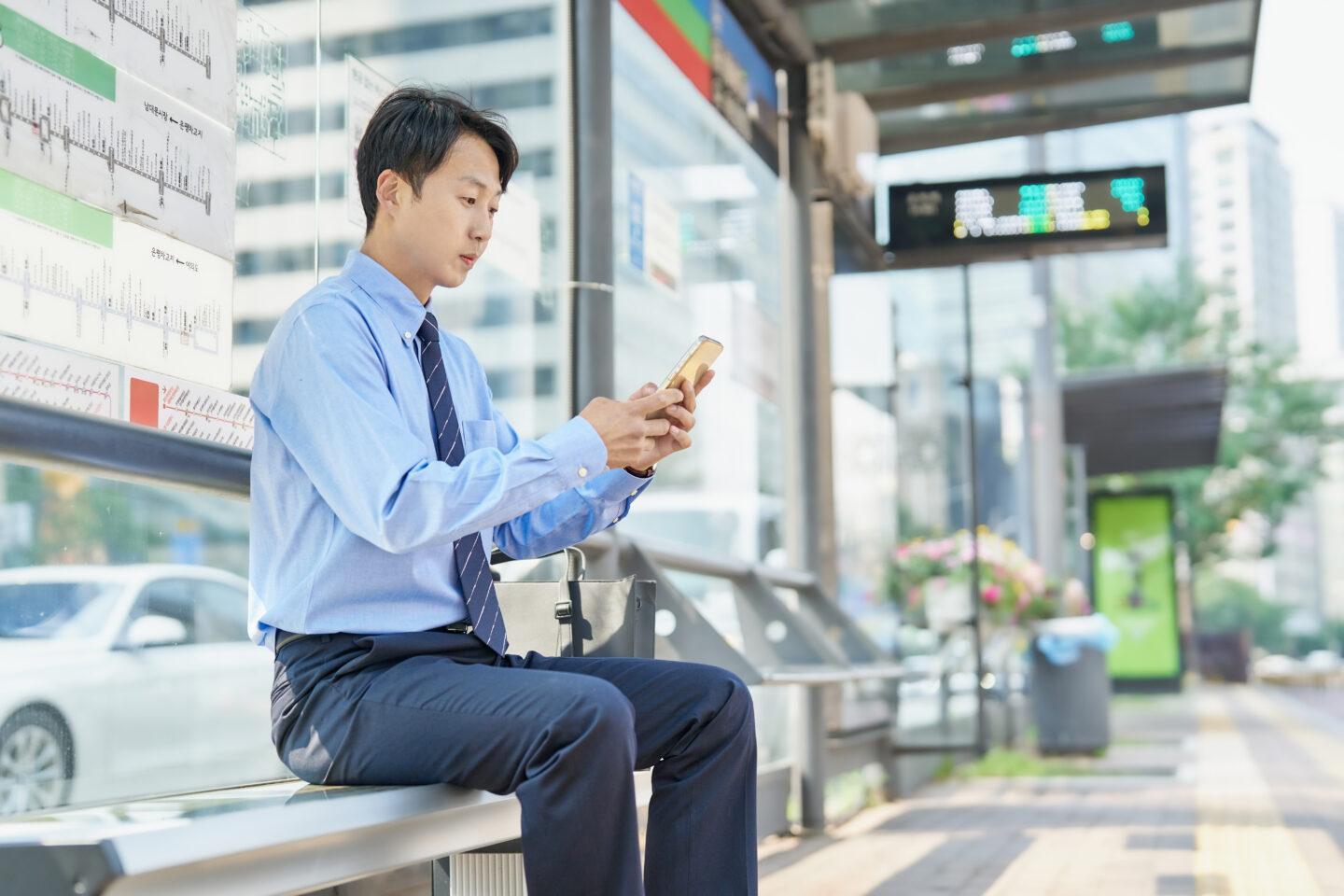 Mężczyzna na nowoczesnym przystanku autobusowym trzyma smartfon