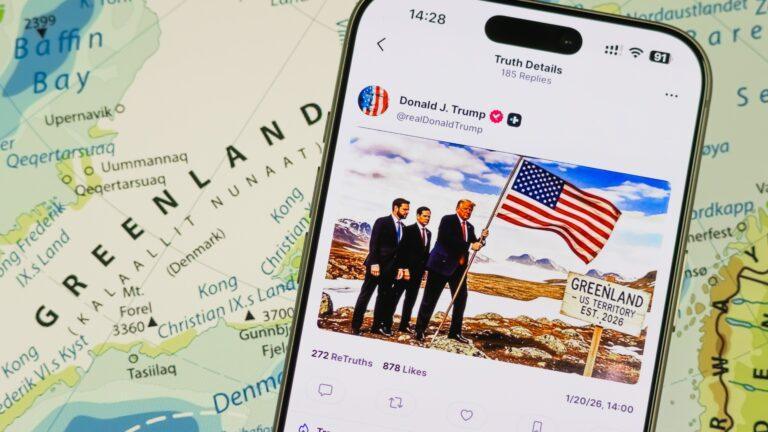 Wpis Donalda Trumpa dotyczący Grenlandii na smartfonie. W tle mapa Grenlandii. Fot. Cheng Xin/Getty Images