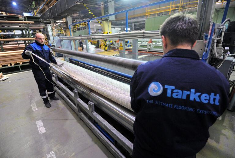 Pracownicy jednej z fabryk grupy Tarkett z rolką wykładziny podłogowej.